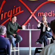 Man and woman speaking at an event in front of a large Virgin Media logo.
