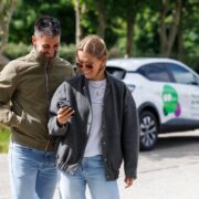 Man and woman looking at smartphone with a car in the background.