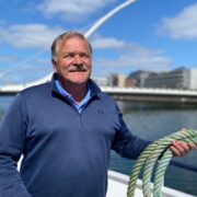 Man in blue sweater holding a rope on board a ship on the River Liffey.