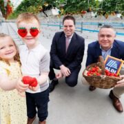 Two children holding strawberries and two men in suits with one holding a basket of strawberries.