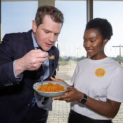 Man tasting food held by woman in white t-shirt.