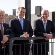 Three men in suits leaning against a railing.