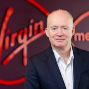 Man in white shirt in front of a Virgin logo.