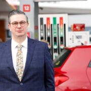 Man in suit standing on a petrol station forecourt.