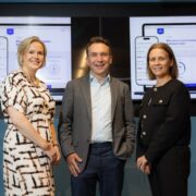 Two women and a man standing in front of screens.