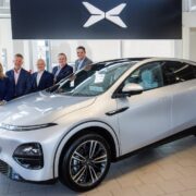 Four men and a woman standing behind a silver electric SUV.
