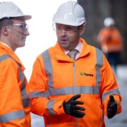 Two men in orange hi-vis jackets and white helmets.
