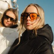 Young women in coats and sunglasses under a blue sky.