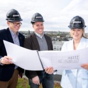 Two men and a woman study building plans on a roof.