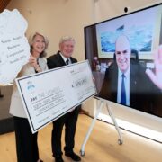 Man and woman holding signs beside a man on a TV screen.