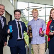 Three men and a woman in a red jacket at an awards ceremony.