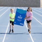 Four kids on a running track with a large version of a bank card.