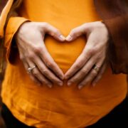 Expectant mother holds hands over belly in love heart gesture.