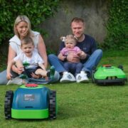 Mother and father with two children and two robot lawn mowers.