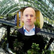 Man inset on image of glass building surrounded by greenery.