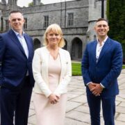 woman in white suit alongside two men in blue suits.