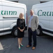 Woman in black business suit beside man in sports jacket.