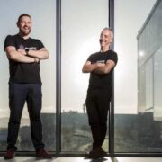 Two men in black in front of a large glass window.