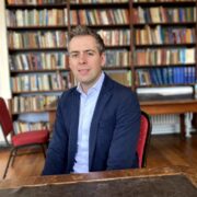 Man in navy suit sitting in a library.
