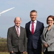 Two men and a woman in front of a wind turbine.