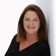 Woman in black dress leaning against a wall.