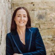 Woman in blue jacket leaning against a wall.