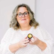 Woman in white sweater holding a skincare product.