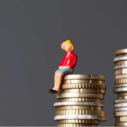 image of a man sitting on a higher stack of coins than a woman.
