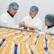 Two men and a woman speaking inside a bakery.