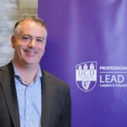 Man in suit before a purple UCD banner.