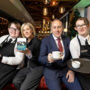 Three women and a man in a hotel holding coffee.