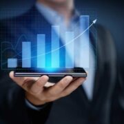 Man holding a smartphone that projects bar charts to denote business growth.