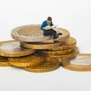 Man reading paper while sitting on a stack of Euro coins.
