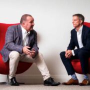 Two men sitting in big red chairs.