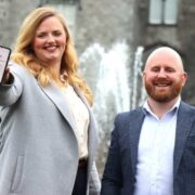 Woman in grey jacket holding a phone beside man in dark sports jacket.