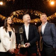 A woman and two men with one of the men holding an award.