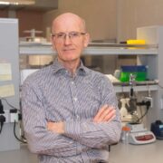 Man standing in lab with arms folded.