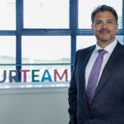 Man wearing suit and purple tie standing in front of a window.