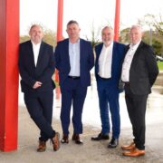Four men in business suits standing among red poles.
