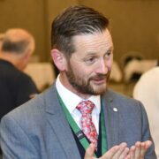 Man in grey suit talking at an event.
