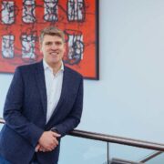 Man in navy jacket leaning against a rail.