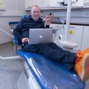 Man with laptop in a dentist's chair. He's waring orange trainers.