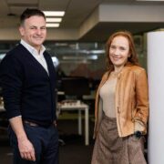 Man in dark sweater beside woman in tan jacket.