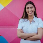 Woman in white t-shirt in front of a colourful wall.