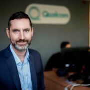 Man in office wearing navy suit with blue shirt.