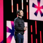 Man wearing black shirt on stage at a conference.