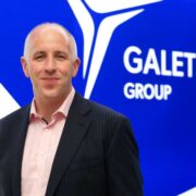 Man in dark suit with salmon shirt.