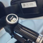 Close-up of a diesel fuel pump nozzle inserted into a vehicle fuel tank, with the cap clearly labelled “Diesel” and the fuel filler door open.