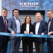 Group of executives standing outside a Kerry biotechnology facility in Carrigaline, holding a branded ribbon during the opening of the expanded site.