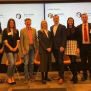 Group of ten adults standing side by side in a conference room in front of two large presentation screens.